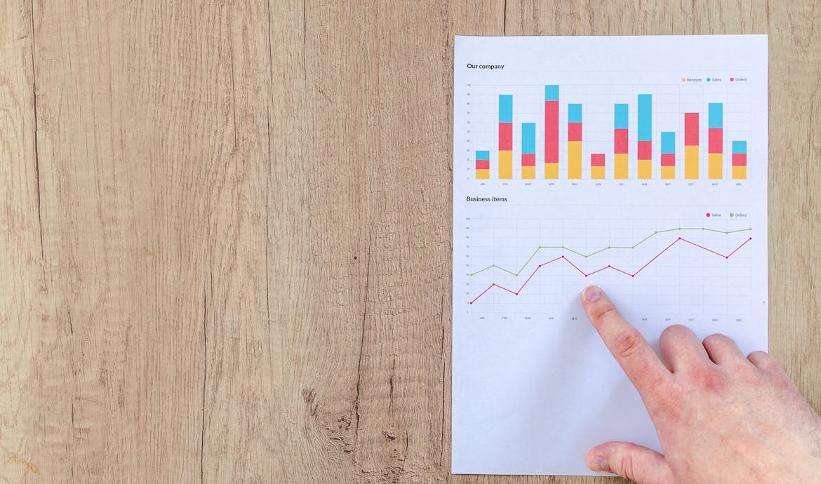 Hand analyzing business graphs on a wooden desk, focusing on data results and growth analysis.