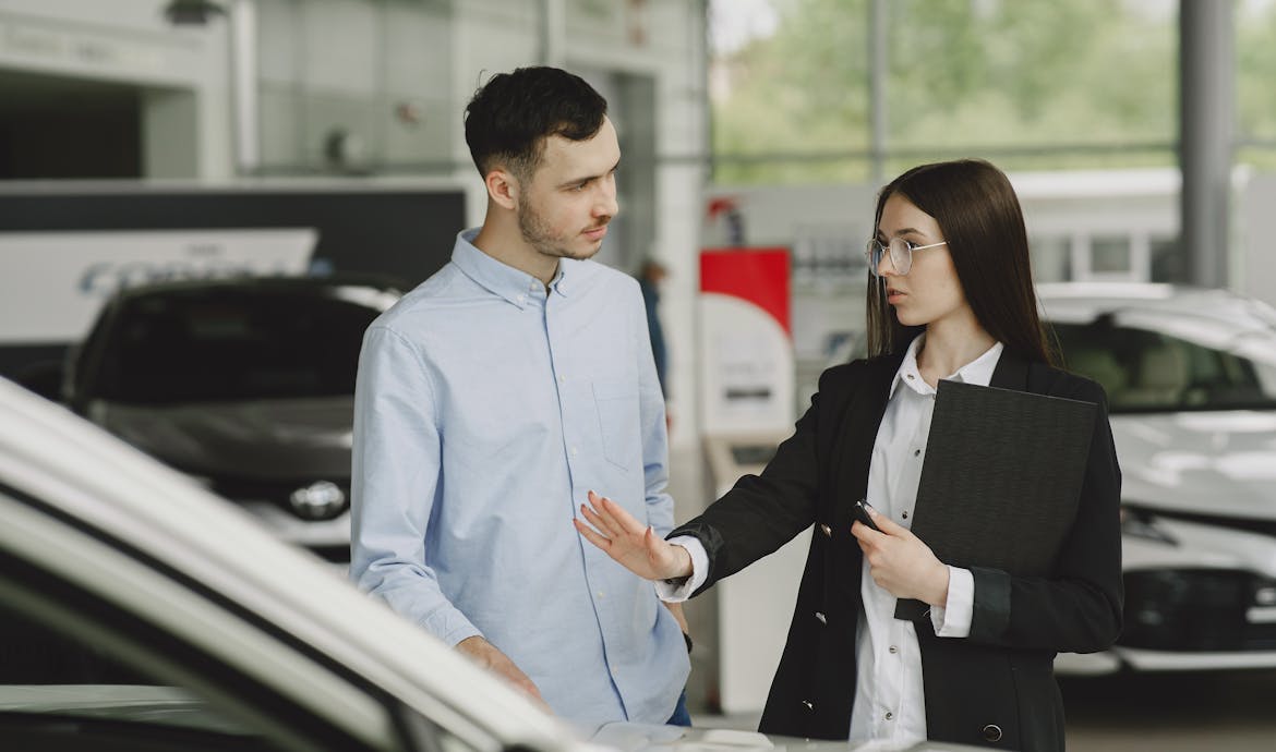 A salesperson and customer discussing car features in a dealership setting.